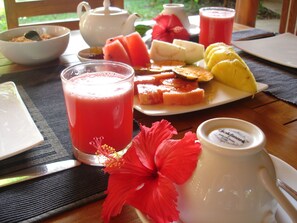 A table with a fruit platter, a glass of red juice, a teapot, and a pitcher of milk. - Kuwera Eco Lodge (Avudangawa)