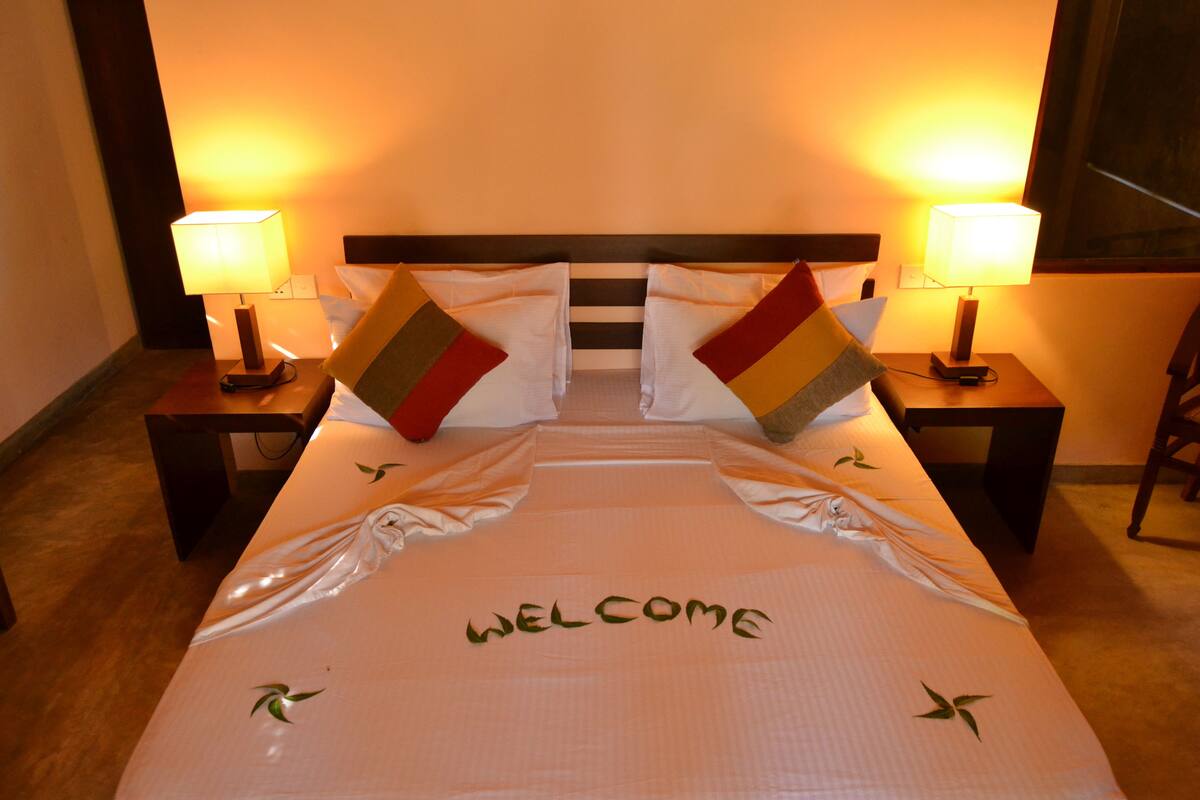 A neatly made bed with a 'WELCOME' sign on the bedspread, two bedside lamps, and a wooden headboard.