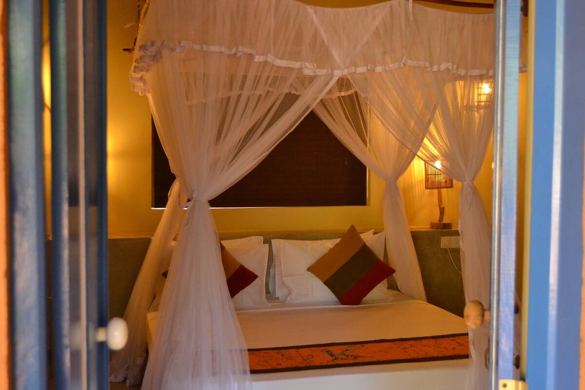 A room with a bed under a canopy, a nightstand, and a wall-mounted lamp.