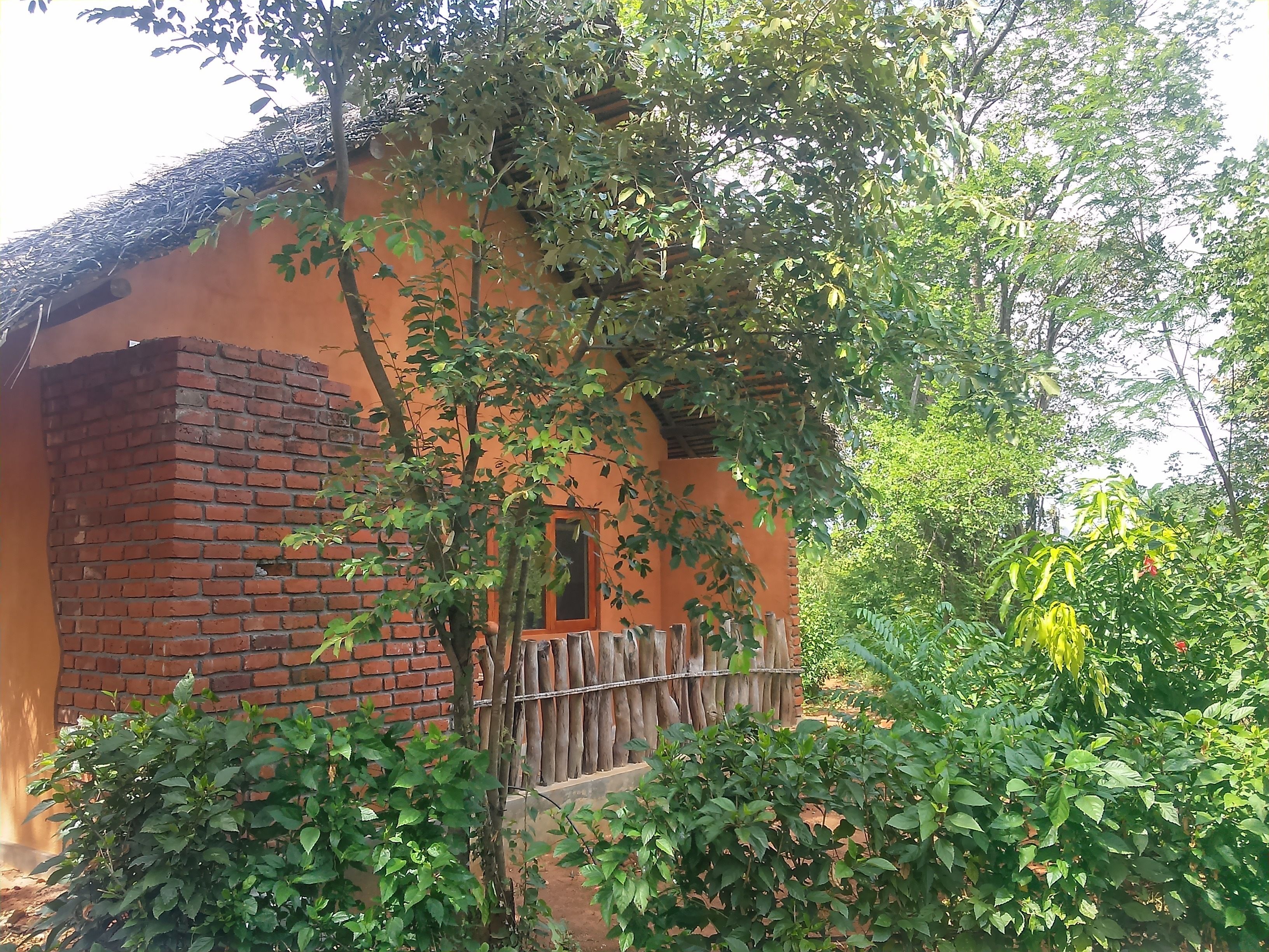 Un edificio rústico con una chimenea de ladrillo, rodeado de exuberante vegetación y una valla de madera.