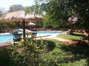 A swimming pool area with a thatched-roof structure, lounge chairs, and surrounding greenery. - Kuwera Eco Lodge (Avudangawa)