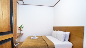 Una cama bien hecha con una manta marrón, almohadas blancas y una colcha de cuadros al pie.