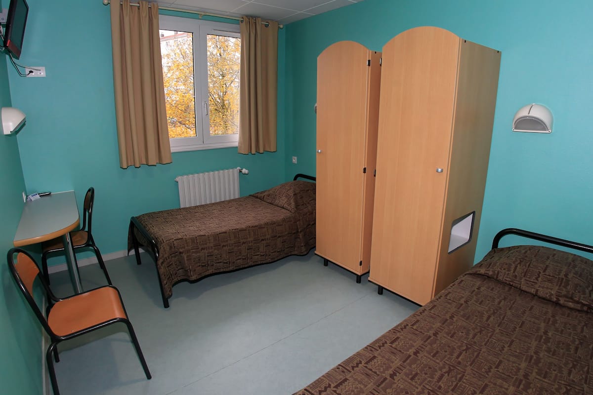 A room with two beds, a table, and a chair.