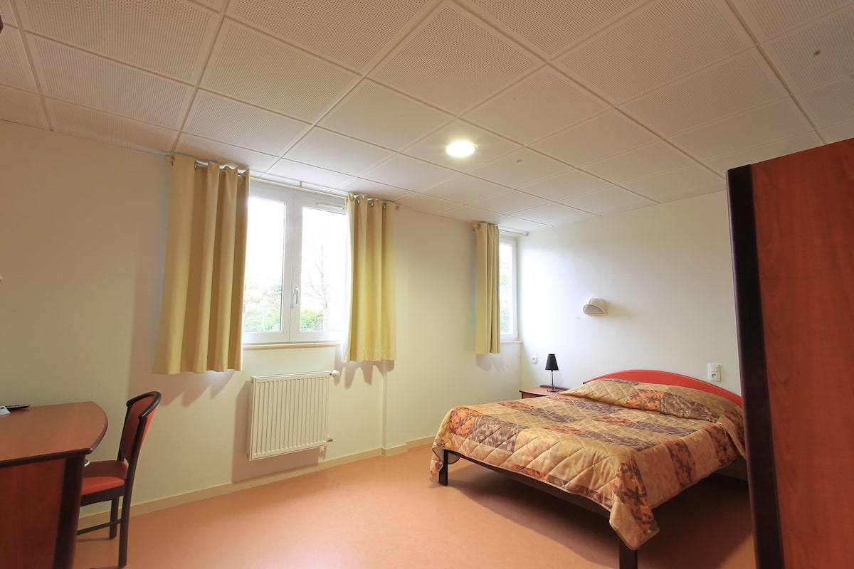 A bedroom with a bed, a chair, a table, and a window with curtains.