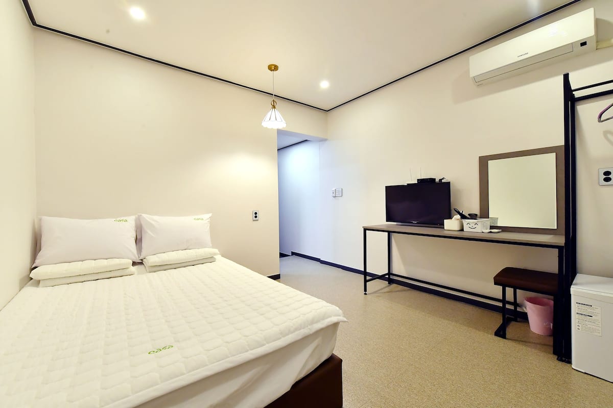 Una habitación de hotel moderna con una cama, un escritorio con ordenador, un espejo y un aire acondicionado.