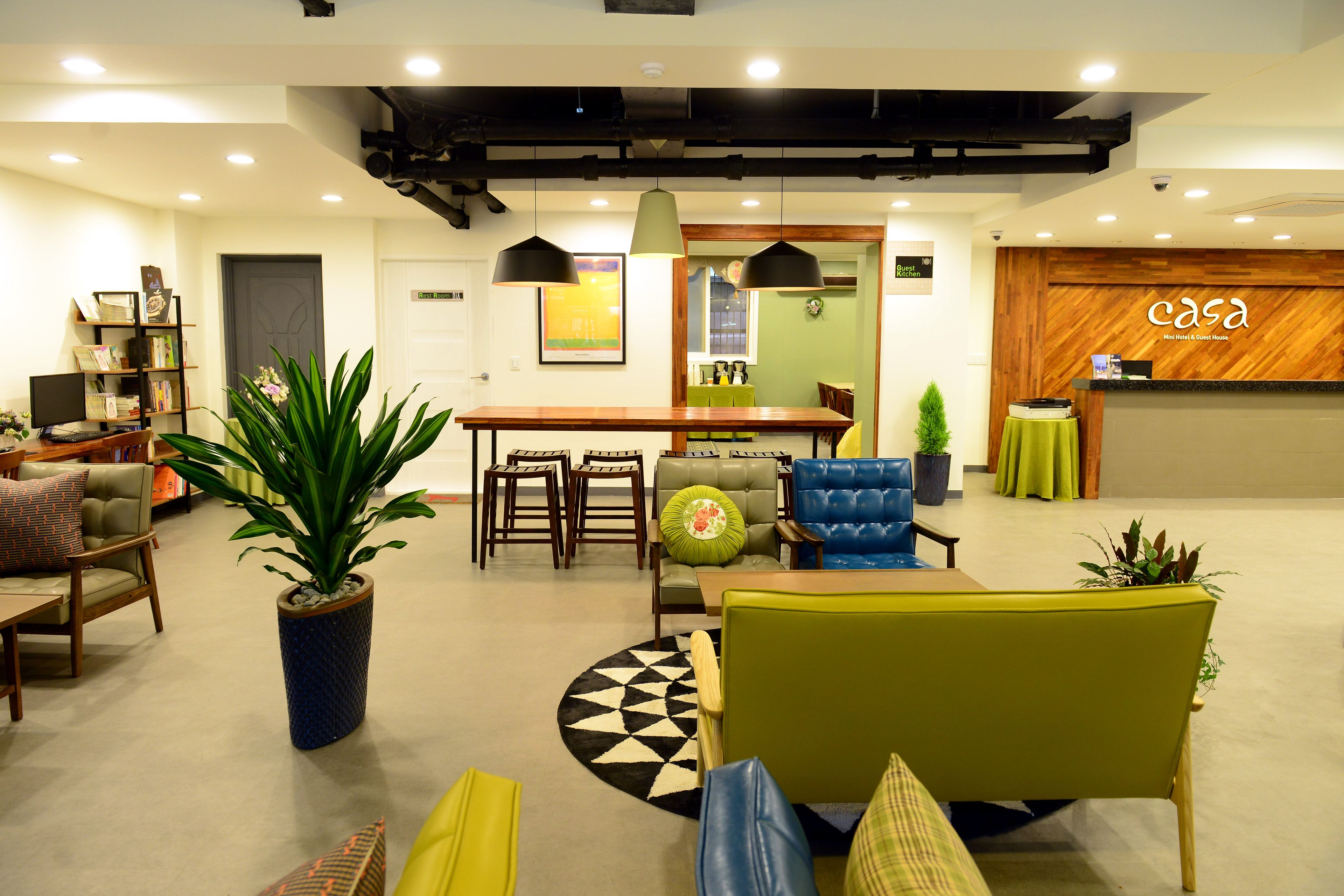 A modern hotel lobby with a reception desk, seating area, and a large potted plant.