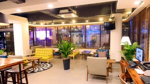 A modern office space with a wooden table, yellow sofa, and multiple chairs. There are potted plants and a computer desk with a monitor and keyboard. - Casa Mini Hotel (Gyeongju)