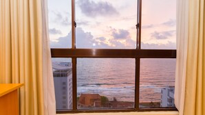 A window with a view of the sea and buildings during sunset.