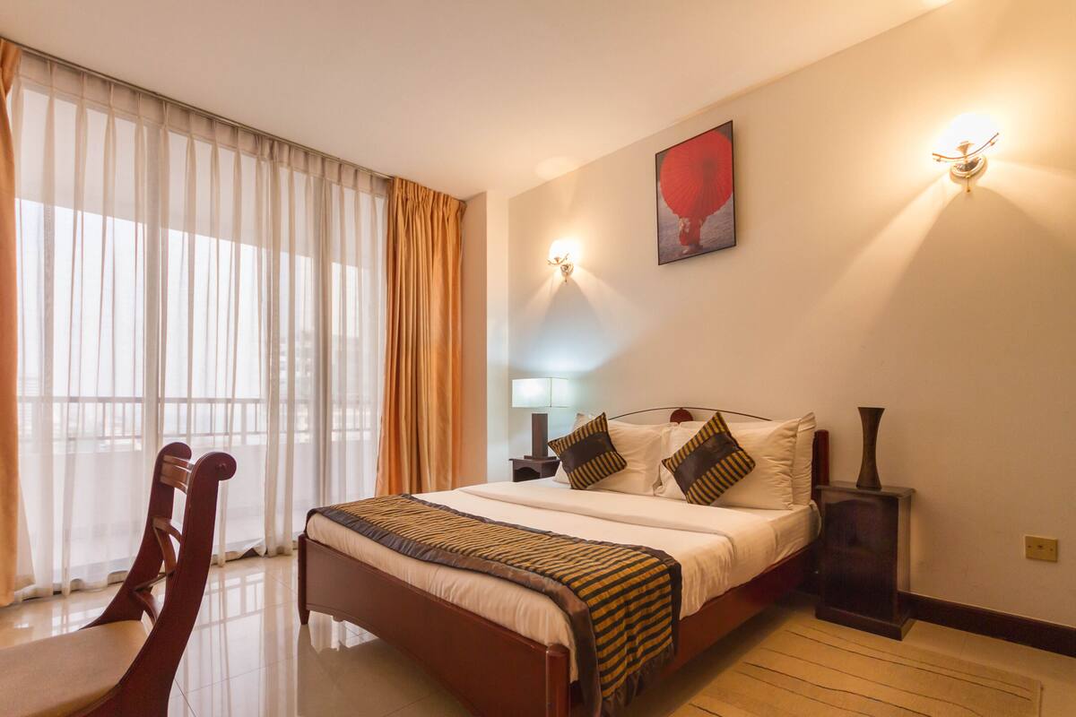 A hotel room with a large bed, a chair, a nightstand, and a lamp.