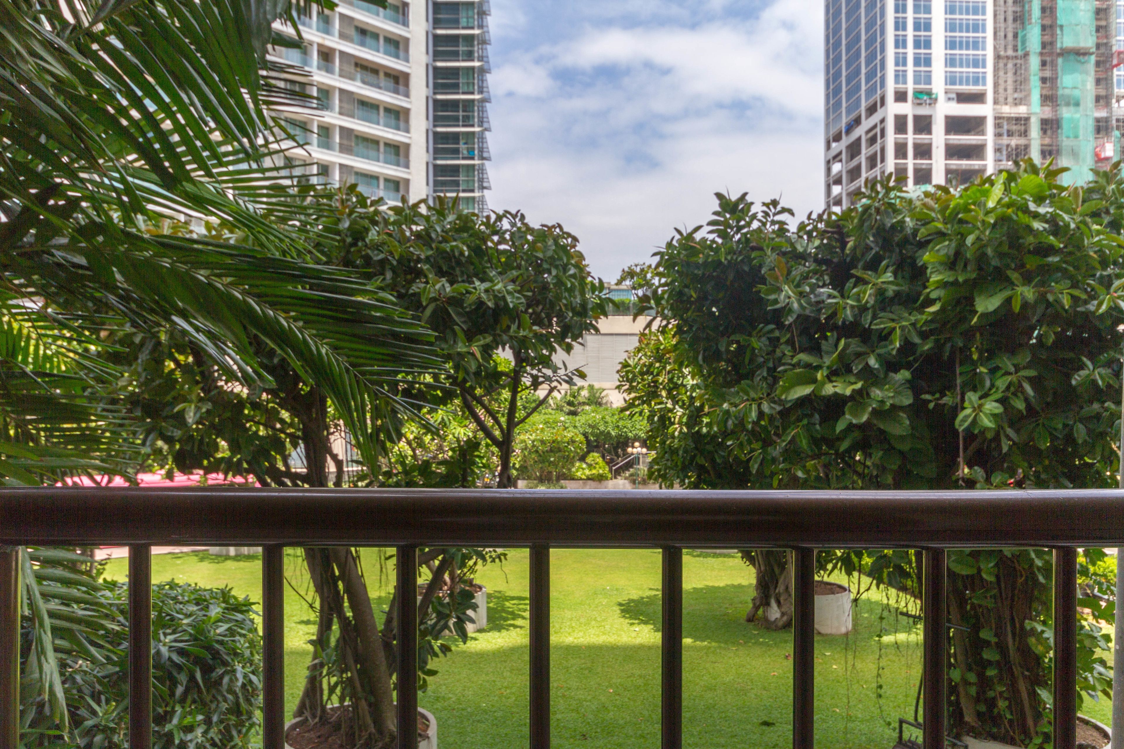 A view of a lush garden with various trees and a well-maintained lawn, seen through a balcony railing.