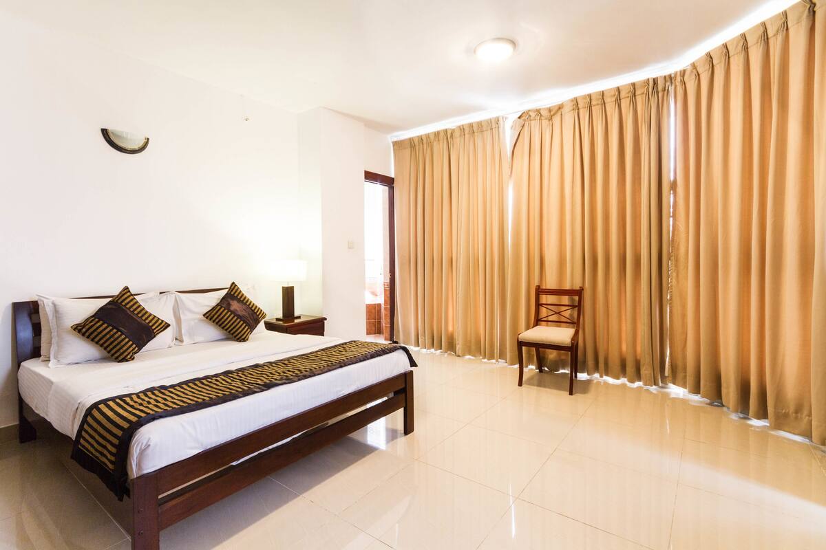 A hotel room with a bed, a chair, curtains, and a nightstand.