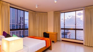 A hotel room with a large bed, a desk, and a view of the sea and buildings.