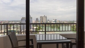 A balcony with a table and chairs, overlooking a cityscape with buildings and a river.
