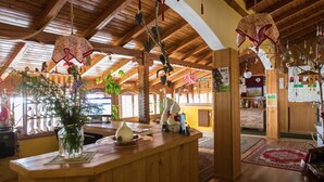 A wooden interior with a reception desk, hanging decorations, and a view of the outside. - Hotel Vecchia America (Dimaro Folgarida)
