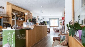 A cozy bar area with wooden shelves stocked with bottles and glasses, a green refrigerator, and a seating area with a sofa and a table. - Hotel Vecchia America (Dimaro Folgarida)