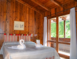 Un dormitorio de cabaña de madera con dos camas, un cuadro en la pared y una ventana con cortinas.