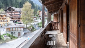 A wooden balcony with a view of a mountain village, including buildings and a road. - Hotel Vecchia America (Dimaro Folgarida)