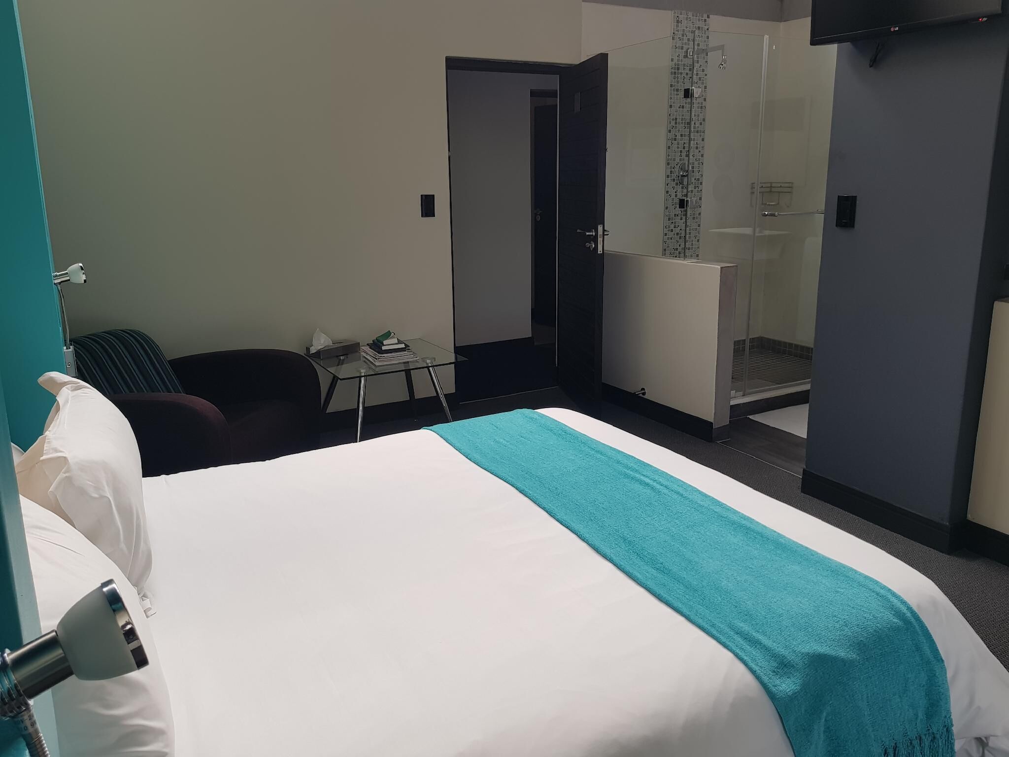 A hotel room with a bed, a desk, a chair, a bathroom with a shower, and a TV mounted on the wall.