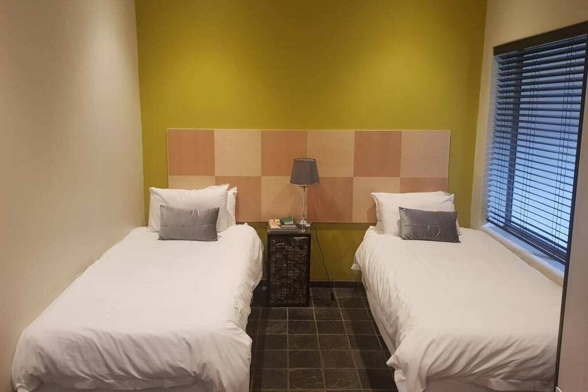 Ett hotellrum med två sängar, en sänggavel med ett rutmönster, ett nattduksbord med en lampa och ett fönster med persienner.