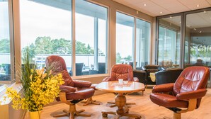 A modern interior with leather chairs, a wooden table, and large windows offering a view of the outdoors. - Almaas Hotell Stord  (Stord)