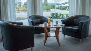 A room with two black leather chairs, a wooden table, and a window with a view of a road and greenery. - Almaas Hotell Stord  (Stord)