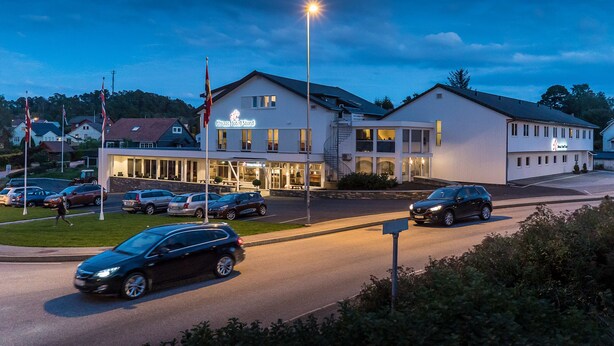 A hotel with a modern design, a parking lot, and a street with cars. - Almaas Hotell Stord  (Stord)