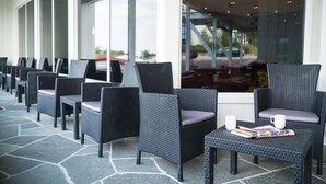 A row of wicker chairs with cushions, arranged on a stone patio outside a building with large windows. - Almaas Hotell Stord  (Stord)