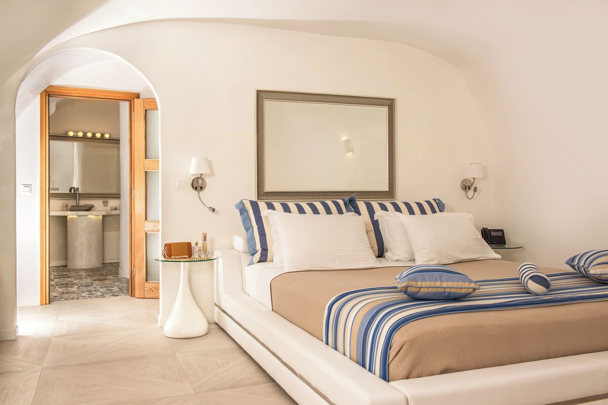 Un dormitorio con una cama grande, un espejo, lámparas de noche y una mesita con lámpara.