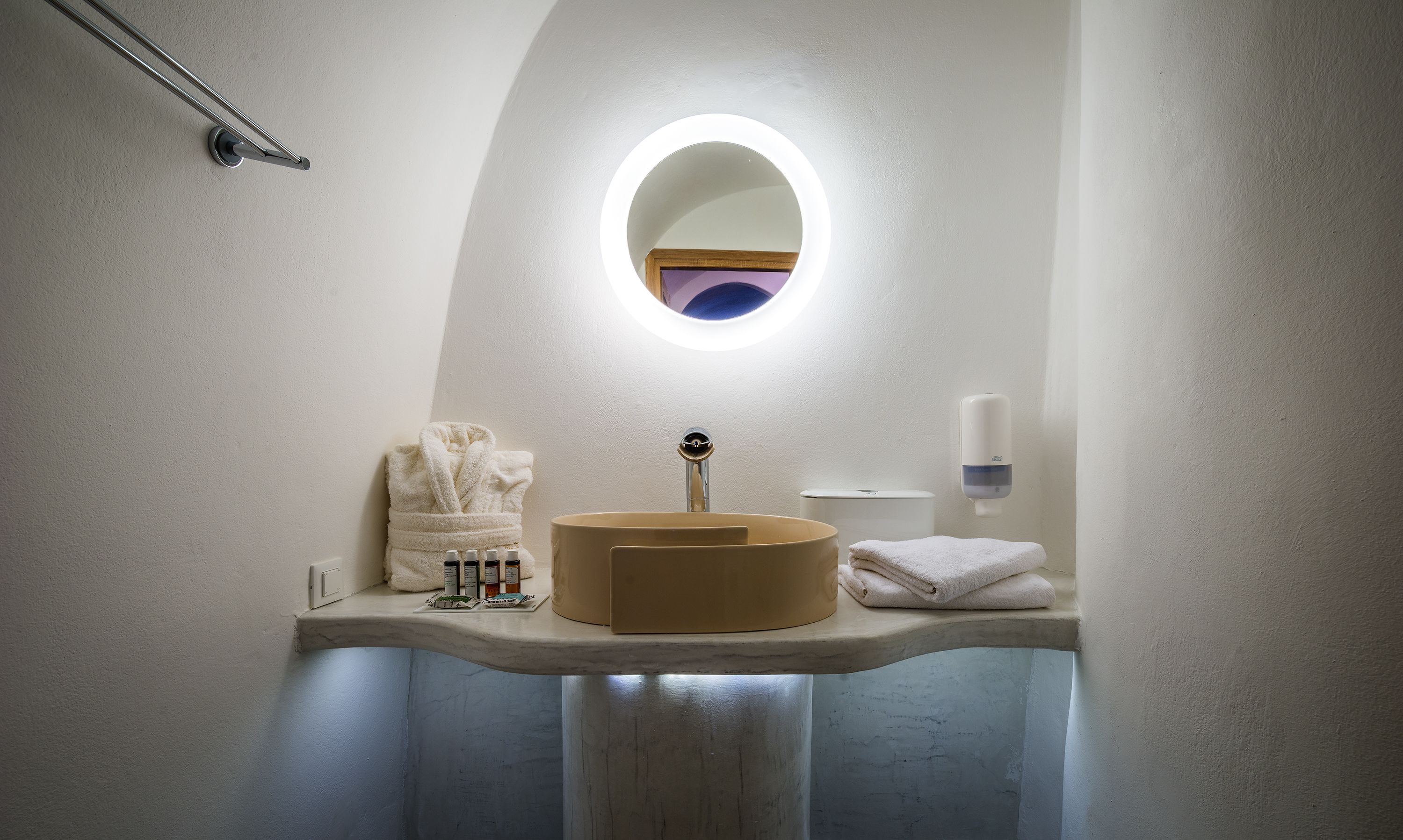 A bathroom with a round mirror, a sink, and a towel rack.