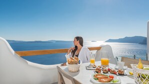 A table set with food and drinks, overlooking a scenic view of the sea and islands. - Elite Luxury Suites (Santorini)