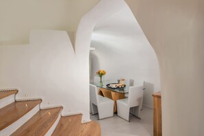 A modern interior with a staircase, a dining area with a glass table, and white chairs. - Elite Luxury Suites (Santorini)