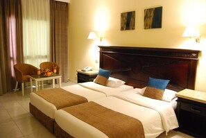 A hotel room with two beds, a chair, a small table with fruit, and a nightstand with a lamp. - Cataract Sharm Resort (Sharm El Sheikh)