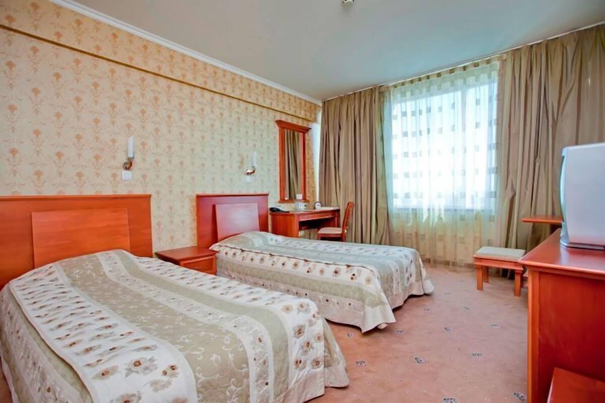 A hotel room with two beds, a desk, a chair, a television, and a window with curtains.