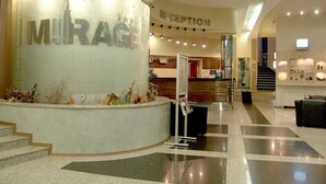 A reception area with a 'Mirage' sign, a reception desk, and a staircase leading to upper floors. - Hotel Mirage (Burgas)