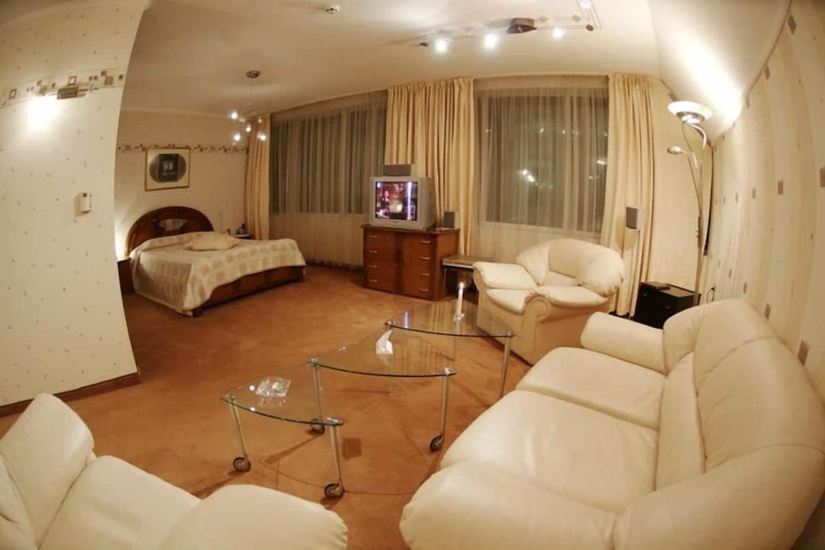 A hotel room with a bed, a sofa, a glass coffee table, and a television.