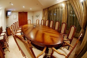 A conference room with a large oval table surrounded by wooden chairs, a television on the wall, and a large window with curtains. - Hotel Mirage (Burgas)