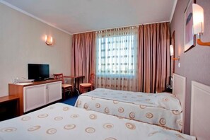 A hotel room with two beds, a desk with a television, and a window with curtains. - Hotel Mirage (Burgas)