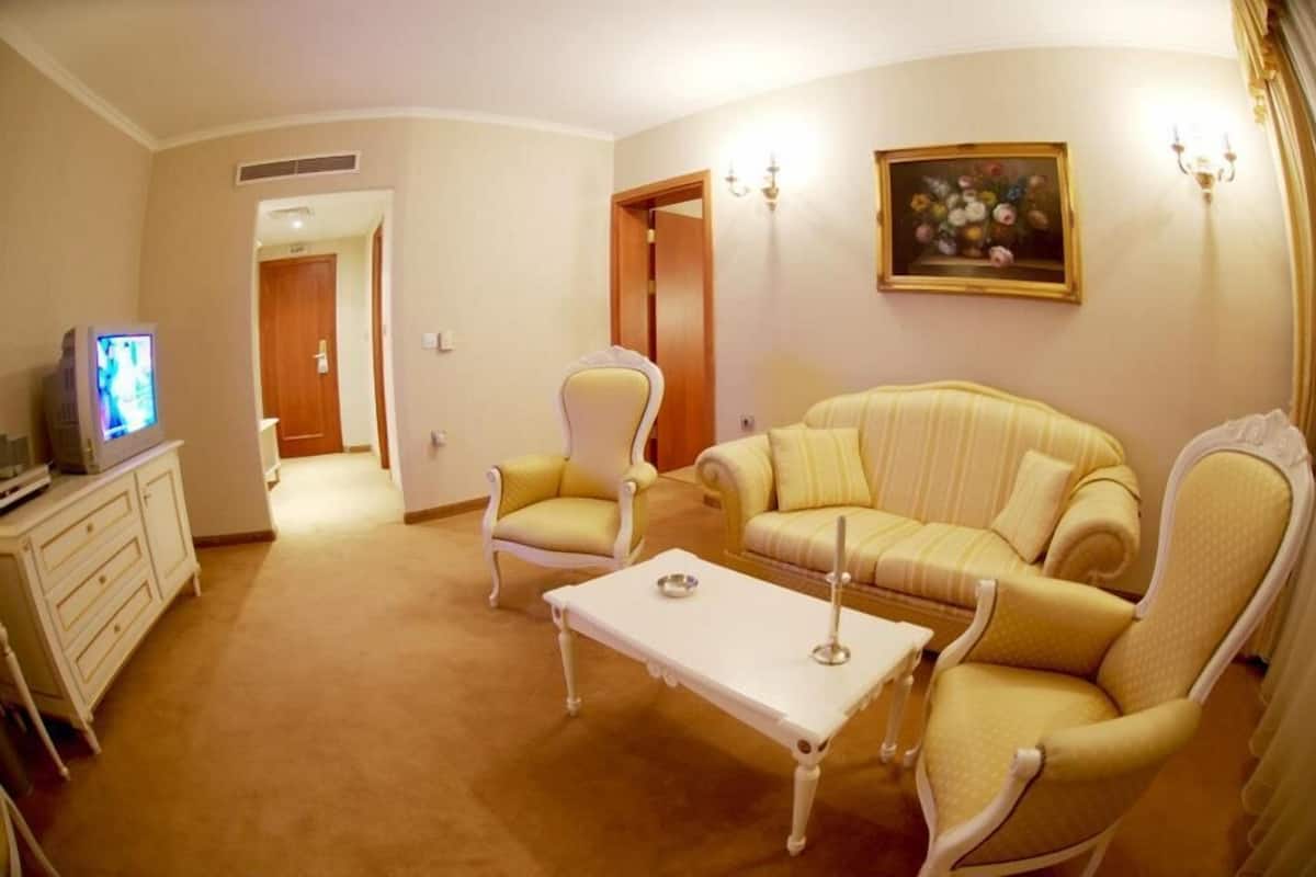 A living room with a sofa, armchairs, a coffee table, a television, and a painting on the wall.