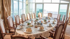 A round dining table set for a meal with chairs, a view of the city through large windows, and a balcony with a railing. - Hotel Mirage (Burgas)