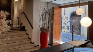 A staircase with a red vase of dried branches, a wooden door with graffiti, and a view of the street outside. - Navona Theatre Hotel (Rome)