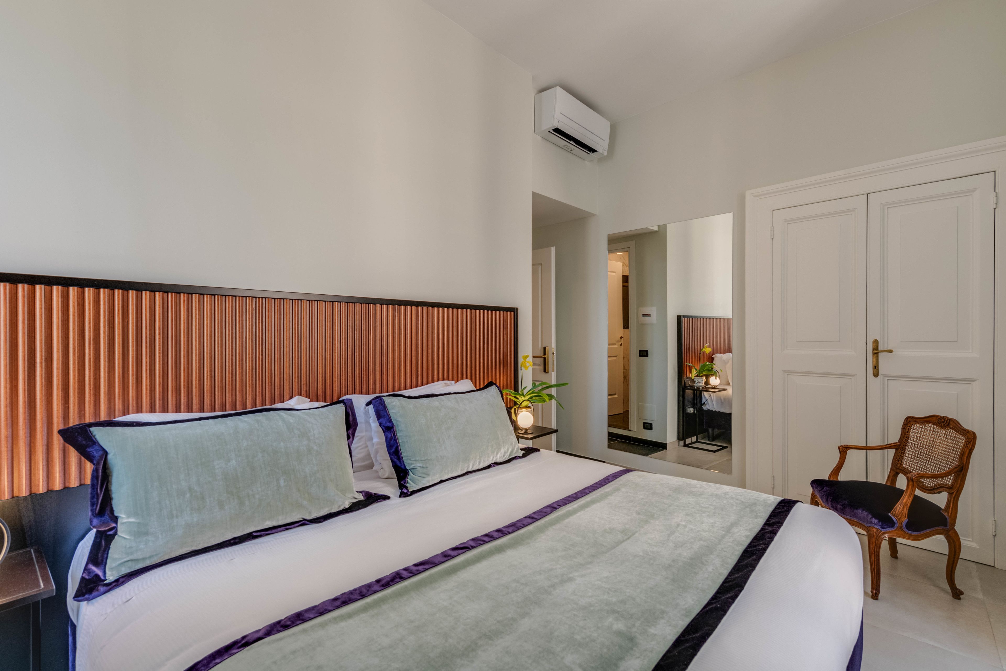 Ein Hotelzimmer mit einem großen Bett, einem Holzkopfteil, einem Sessel und einer Tür zu einem weiteren Raum.