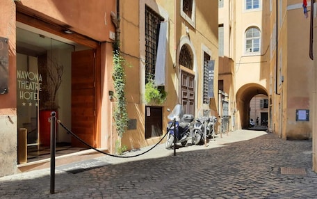 A cobblestone street with a hotel entrance, a motorcycle parked outside, and a pedestrian pathway.