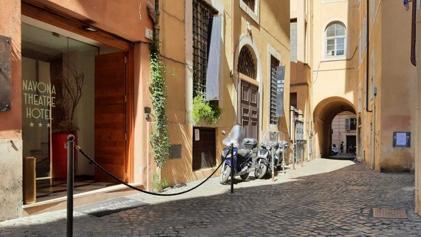 A cobblestone street with a hotel entrance, a motorcycle parked outside, and a pedestrian pathway. - Navona Theatre Hotel (Rome)