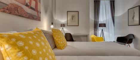 A hotel room with a large bed, two yellow pillows, a desk with a chair, a lamp, and a painting on the wall.