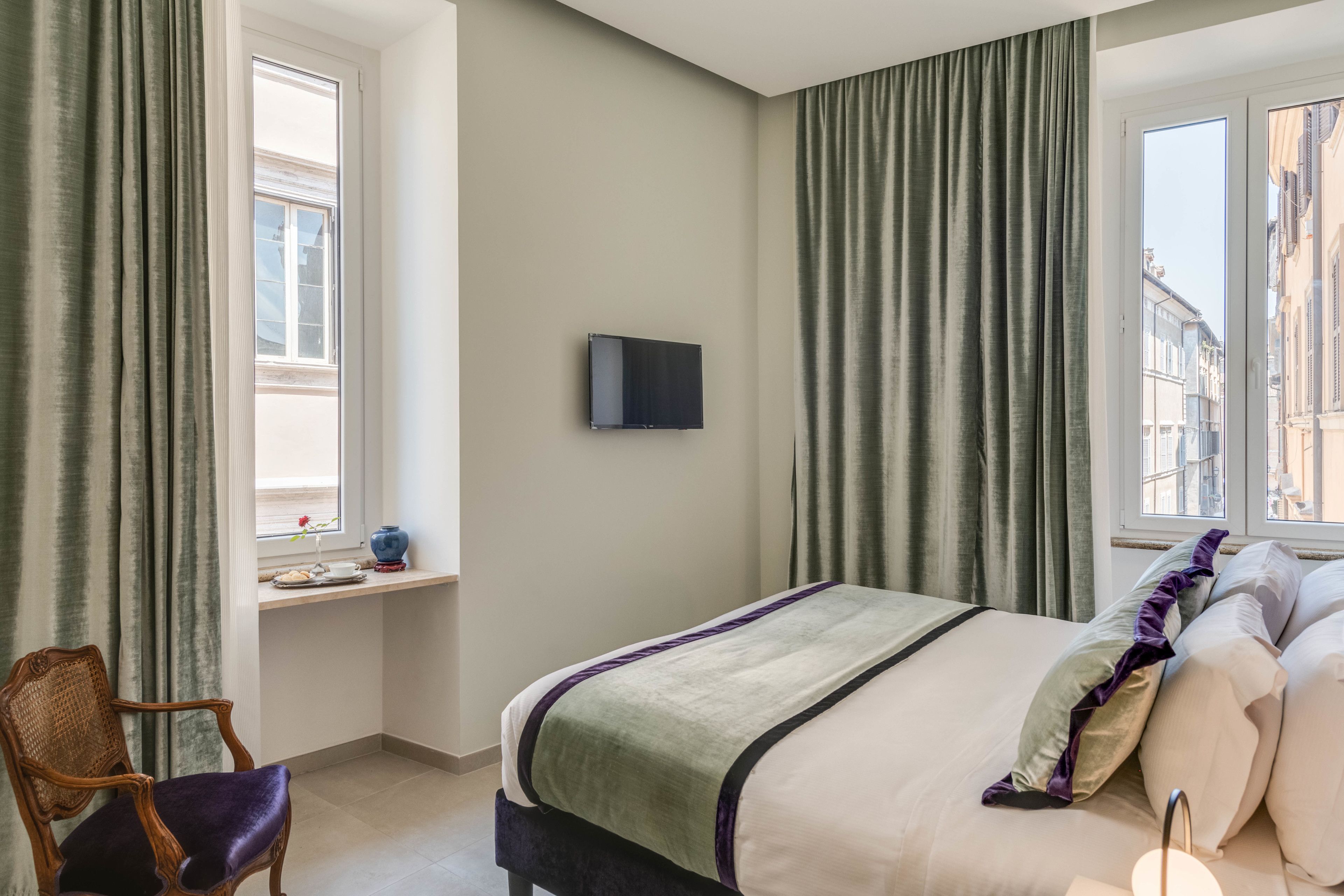 A hotel room with a bed, a chair, a TV, and a window with curtains.