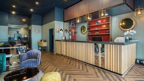 A modern reception area with a wooden reception desk, a blue chair, and a herringbone patterned floor. - Dansaert Hotel (Brussels)