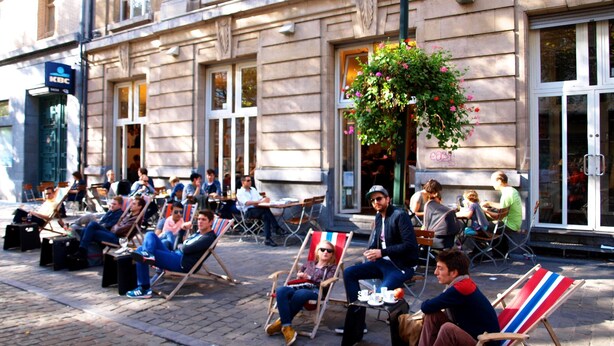 A group of people sitting on outdoor chairs in front of a building with large windows and a KBC sign. - Dansaert Hotel (Brussels)