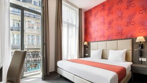 A hotel room with a large bed, a chair, a nightstand with a lamp, and a view of a building through a window. - Dansaert Hotel (Brussels)