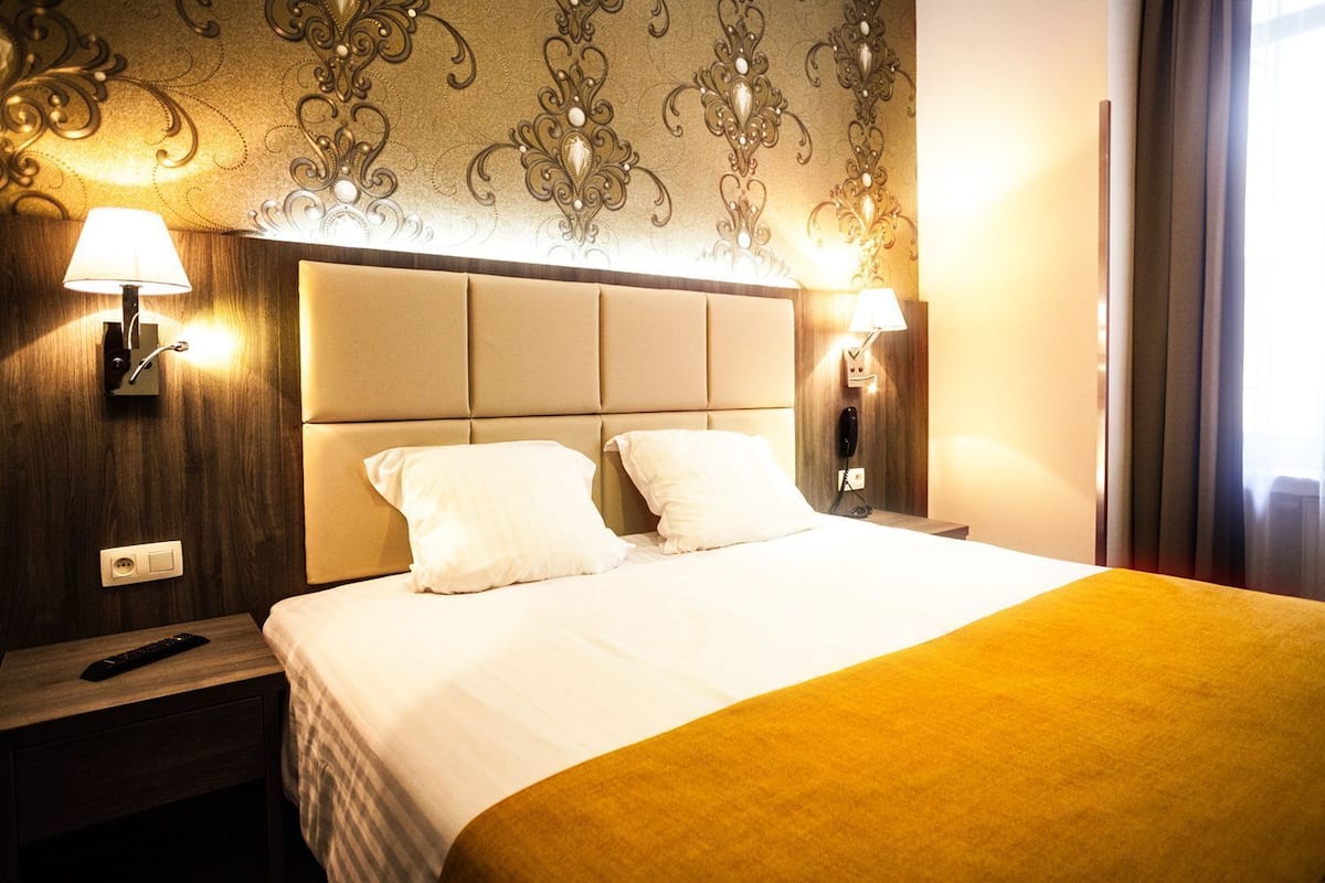Una habitación de hotel con una cama grande, dos lámparas de noche, una mesita de noche y un adorno en la pared.