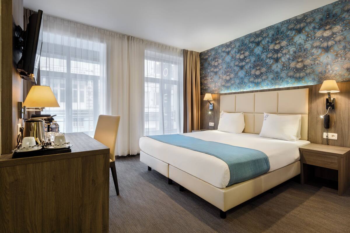 Habitación de hotel con cama, escritorio, teléfono, silla y televisor.